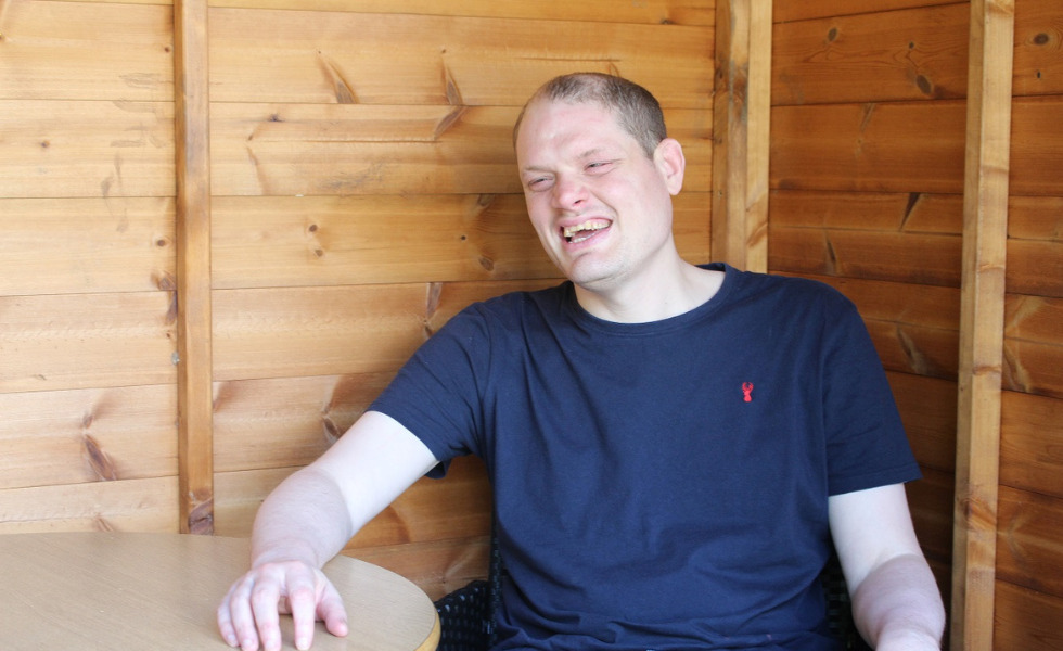 One of Southdown's learning disability clients is sat laughing in their wooden summer house.