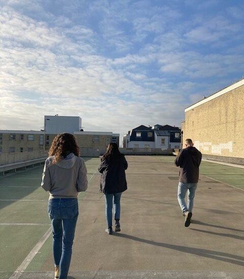 Three people are on the top floor of a multi-storey car park. The sky is blue.