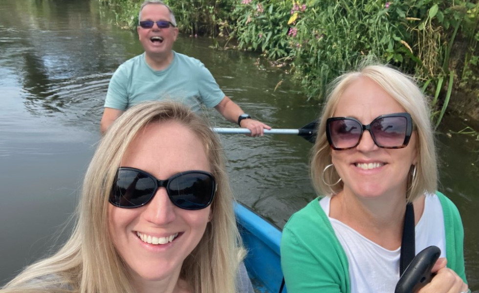 Three Southdown colleagues are rowing on a boat in a river. All three are looking at the camera smiling.