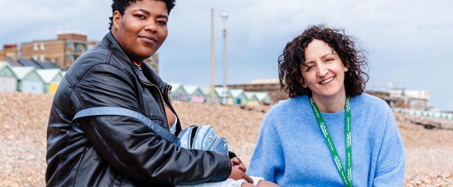 A Southdown colleague and tenant are sitting on the beach and smiling at the camera.