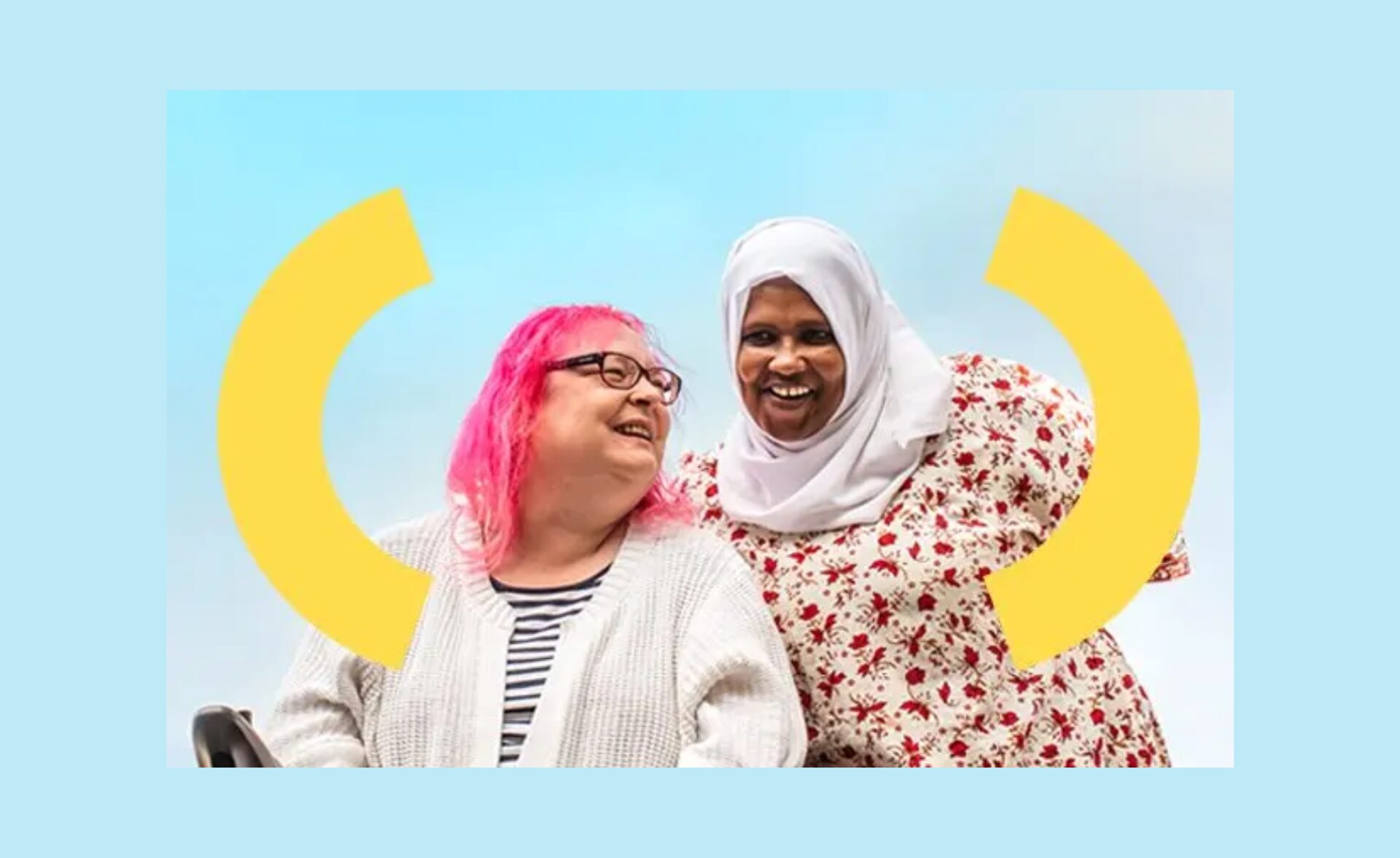 Two women smiling together against a blue sky background, with yellow curved shapes framing them. One woman has bright pink hair, glasses, and is wearing a white cardigan. The other woman is wearing a white headscarf and a floral dress. They appear happy and relaxed, sharing a joyful moment.