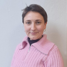 A woman's crop shot with short hair with pink jumper on, against a white wall as background