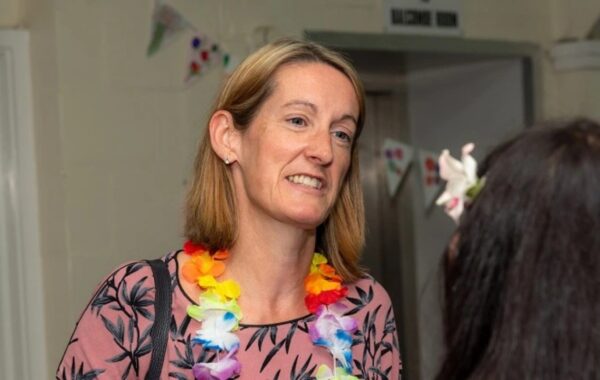 A woman with short blond hair looking slightly sideways into the camera with a plastic floral garland.