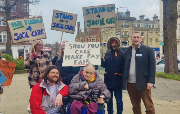 A group of Southdown employees accompanied by a client stand outside Hove town hall with placards asking for fair funding for social care from the local council.