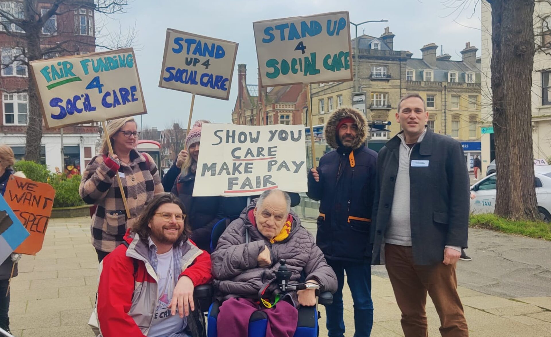 A group of Southdown employees accompanied by a client stand outside Hove town hall with placards asking for fair funding for social care from the local council.